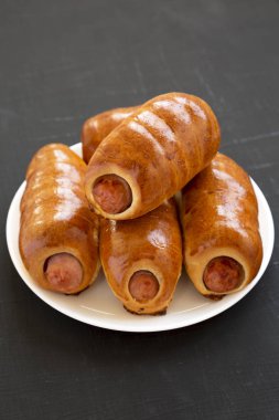 Siyah bir backgr üzerinde beyaz bir tabak üzerinde ev yapımı sığır sosis kolache