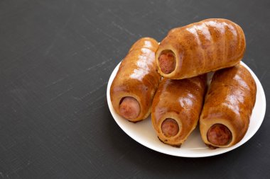 Siyah bir backgr üzerinde beyaz bir tabak üzerinde ev yapımı sığır sosis kolache