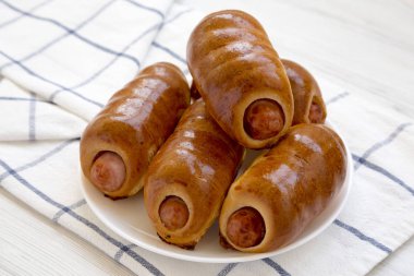 Beyaz bir ahşap üzerinde beyaz bir tabak üzerinde ev yapımı sığır sosis kolache