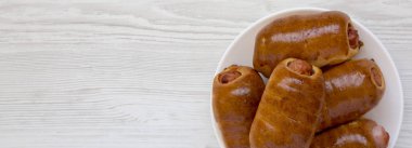 Beyaz bir ahşap üzerinde beyaz bir tabak üzerinde ev yapımı sığır sosis kolache