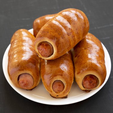 Siyah bir backgr üzerinde beyaz bir tabak üzerinde ev yapımı sığır sosis kolache