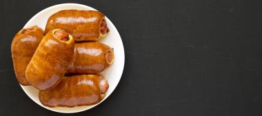 Siyah bir surfac üzerinde beyaz bir tabak üzerinde ev yapımı sığır sosis kolache