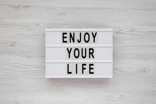 "Genießen Sie Ihr Leben" steht auf einem Leuchtkasten über weißem Holzboden. — Stockfoto