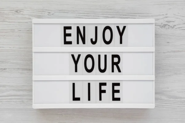 Palabras de "disfruta de tu vida" en un tablero moderno sobre una espalda de madera blanca — Foto de Stock