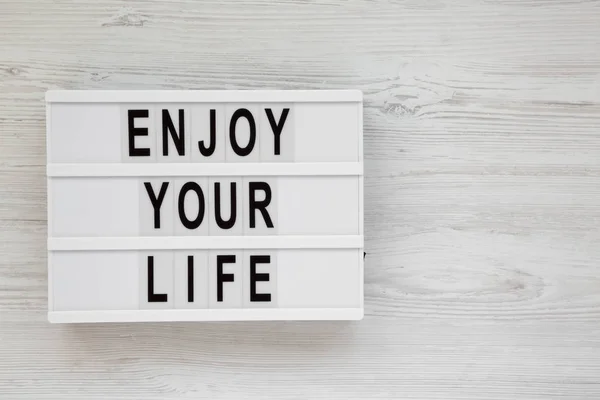 'Enjoy your life' words on a modern board over white wooden back — Stock Photo, Image