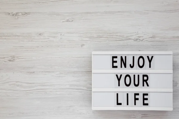 'Disfruta de tu vida' palabras en una caja de luz sobre una superficie de madera blanca , — Foto de Stock