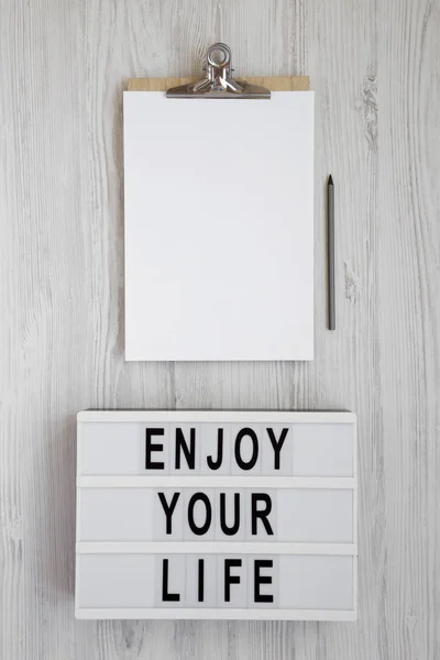 "Genießen Sie Ihr Leben" steht auf einem Leuchtkasten über weißem Holzboden. — Stockfoto
