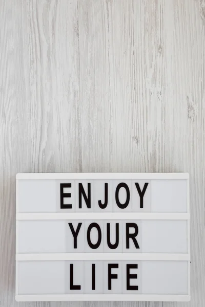 'Disfruta de tu vida' palabras en una caja de luz sobre una superficie de madera blanca , — Foto de Stock