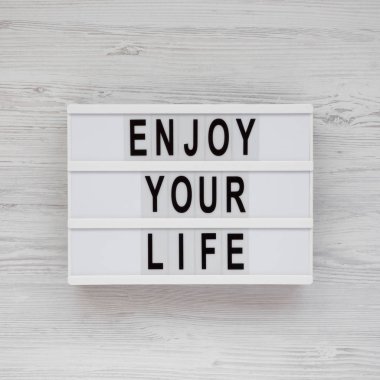 Beyaz ahşap sörf üzerinde modern bir tahta üzerinde 'Enjoy your life' kelimeleri