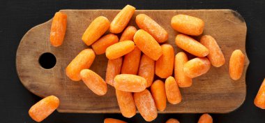 Siyah bir yüzey üzerinde rustik ahşap tahta üzerinde soyulmuş bebek havuç,