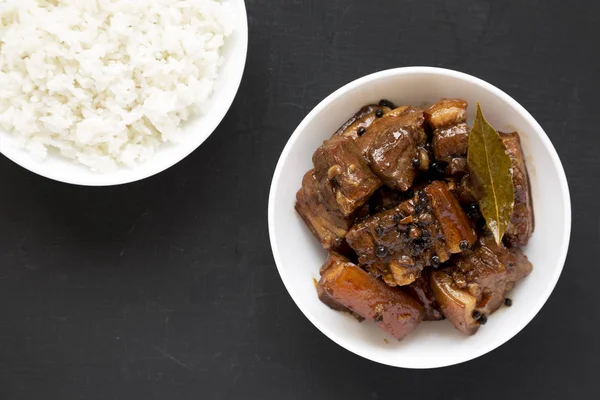 Hausgemachtes philippinisches Adobo-Schweinefleisch mit Reis auf einer schwarzen Holzoberfläche — Stockfoto