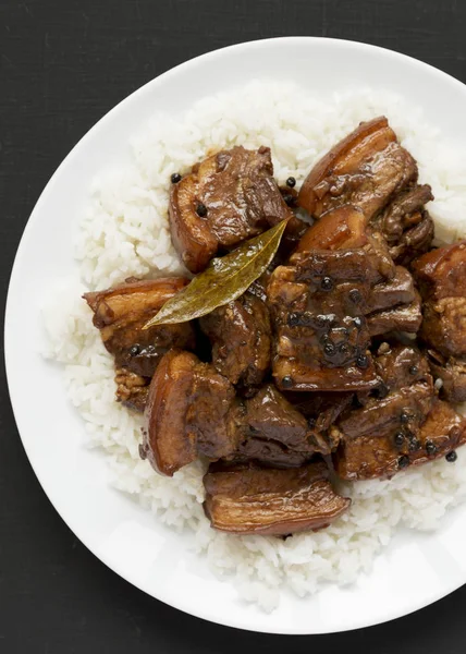 Porco adobo filipino caseiro com arroz em um prato branco em um bla — Fotografia de Stock