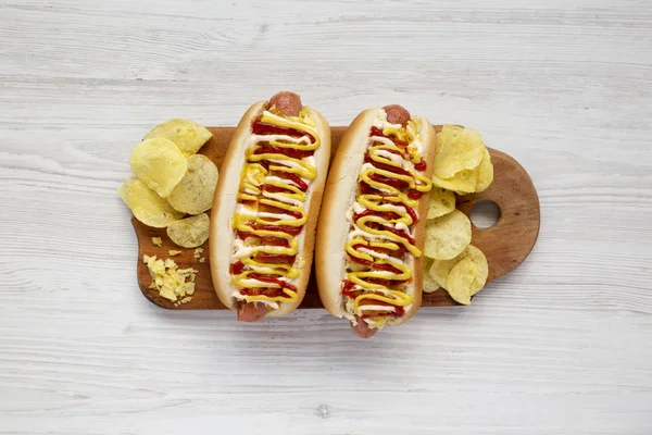 Homemade colombian hot dogs with pineapple sauce, yellow mustard and mayo ketchup on a rustic wooden board on a white wooden surface. Flat lay, from above, top view.