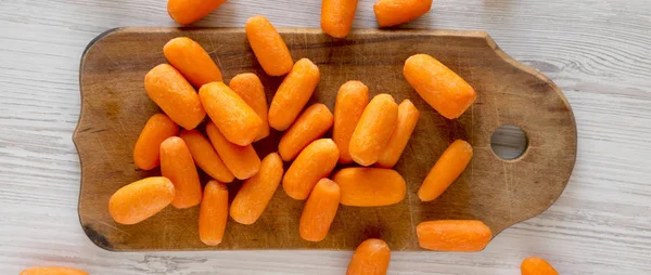 Fresh baby carrots on a rustic wooden board on a white wooden su — Stock Photo, Image