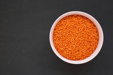 Siyah arka planda pembe bir kasede kırmızı mercimek, üst manzara. Düz