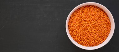 Siyah bir yüzey üzerinde pembe bir kasede kırmızı mercimek, üst manzara. Düz la