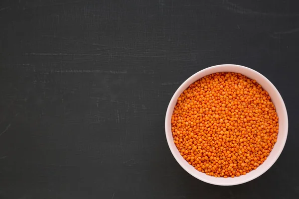 Red lentils in a pink bowl on a black surface, top view. Flat la — Stock Photo, Image