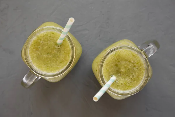 Homemade green cucumber apple smoothie in a glass jar on a concr