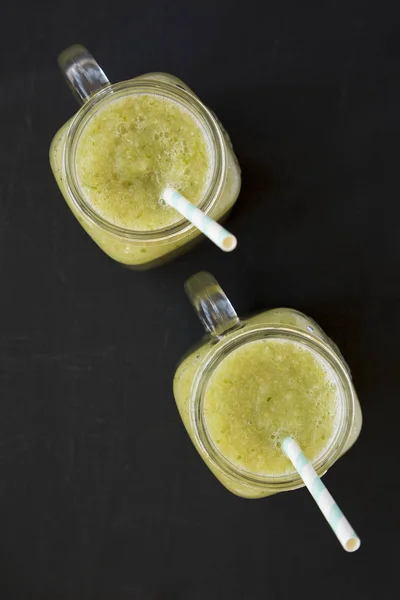 Homemade green cucumber apple smoothie in a glass jar on a black