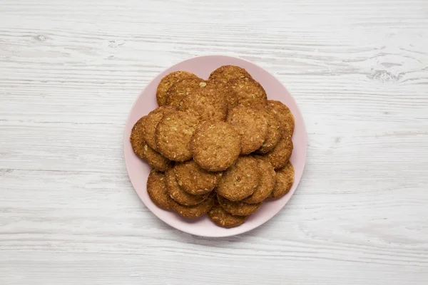 Cereal cookies on a pink plate on a white wooden surface, top vi