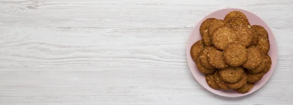 Cereal cookies on a pink plate on a white wooden background, top