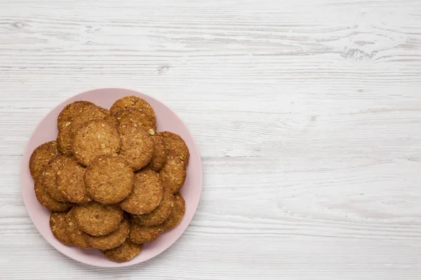 Cereal cookies on a pink plate on a white wooden background, ove