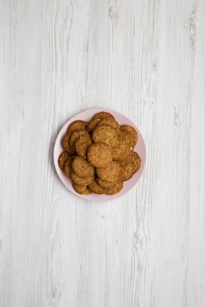 Cereal cookies on a pink plate on a white wooden background, top