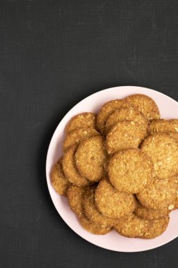 Siyah bir yüzey üzerinde pembe bir tabakta mısır gevreği kurabiyesi, üst manzara. Fla