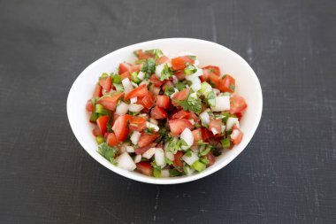 Pico de Gallo siyah arka planda beyaz bir kasede, yan görünüm. 