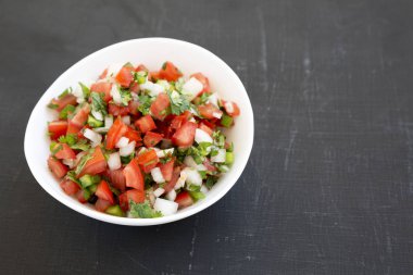Pico de Gallo siyah arka planda beyaz bir kasede, V açısı düşük.