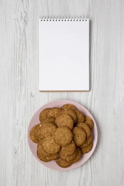 Cereal cookies on a pink plate, blank notepad on a white wooden