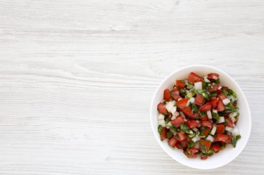 Pico de Gallo beyaz bir kase içinde beyaz ahşap arka planda, en üstte. 