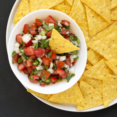 Siyah bir yüzey üzerinde glütensiz tortilla cipsli Pico de Gallo.