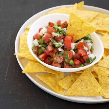 Siyah bir yüzey üzerinde glütensiz tortilla cipsli Pico de Gallo.