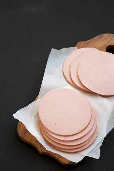 Sliced pork bolgna meat on a rustic wooden board on a black surf — Stock Photo, Image