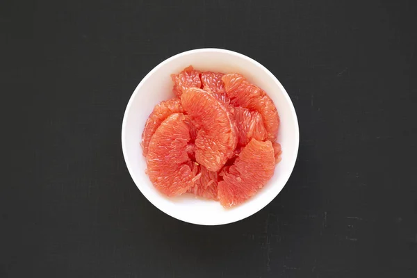 Red grapefruit slices in a white bowl on a black background, top
