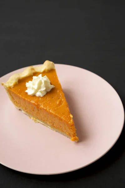 Homemade Thanksgiving pumpkin pie on a pink plate on a black sur — Stock Photo, Image