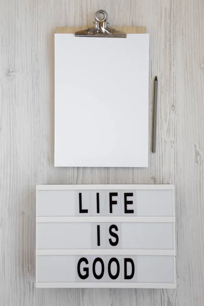 \'Life is good\' words on a lightbox, clipboard with blank sheet o