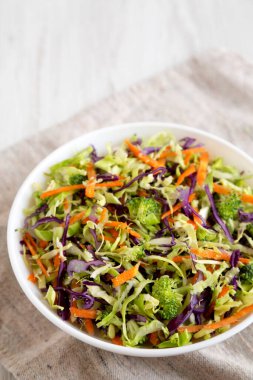 Beyaz ahşap arka planda beyaz bir kâse içinde ev yapımı çiğ brokoli salatası. Metin için boşluk.