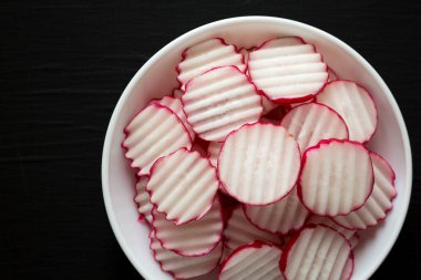 Taze turp cipsleri siyah arka planda beyaz bir kasede dilimler. Düz yatıyordu, üstten, yukarıdan. Metin için boşluk.