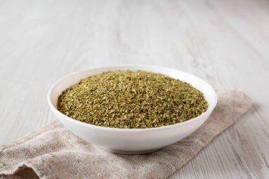 Kurumuş yeşil Yunan Oregano Baharatı beyaz bir kâse içinde ahşap arka planda, yan görünüm. 