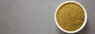 Kurumuş yeşil Yunan Oregano Baharatı gri bir yüzey üzerinde beyaz bir kasede, üst manzara. Dümdüz, tepeden, yukarıdan. Metin için boşluk.