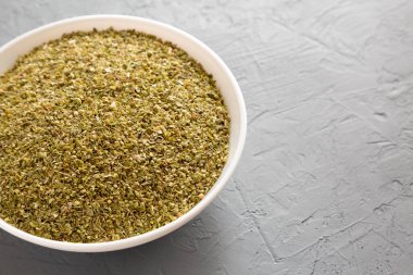 Kurumuş yeşil Yunan Oregano Baharatı gri arka planda, düşük açılı beyaz bir kâsede. Metin için boşluk.
