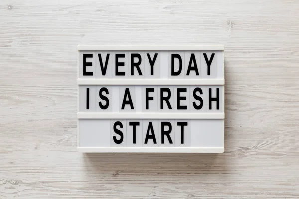 \'Every day is a fresh start\' words on a lightbox on a white wooden surface, top view. Overhead, from above, flat lay.