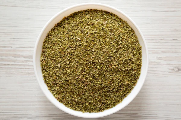 Dried Green Greek Oregano Spice in a white bowl, top view. Flat lay, overhead, from above. Close-up.