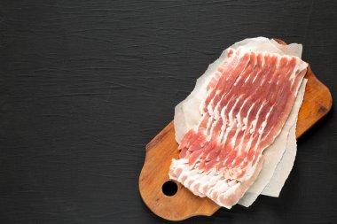 Siyah arka planda, ahşap bir tahtanın üzerinde pişmemiş çiğ domuz pastırması. Dümdüz yatıyordu, yukarıdan, yukarıdan. Boşluğu kopyala.