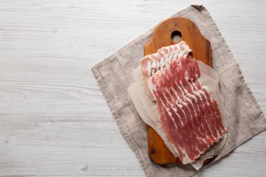 Beyaz ahşap arka planda, ahşap bir tahtanın üzerinde pişmemiş çiğ domuz pastırması. Düz yatıyordu, yukarıdan, yukarıdan. Boşluğu kopyala.