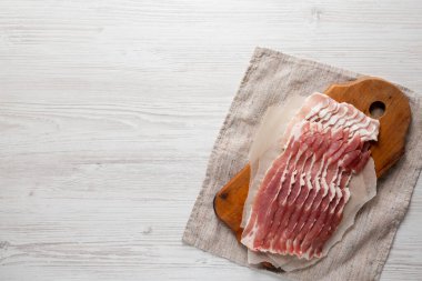 Beyaz ahşap bir yüzeyde, ahşap bir tahtanın üzerinde pişmemiş çiğ domuz pastırması. Düz yatıyordu, yukarıdan, yukarıdan. Boşluğu kopyala.