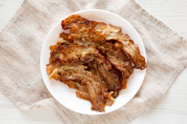 Beyaz ahşap arka planda beyaz bir tabakta ev yapımı domuz pastırması. Yukarıdan, dümdüz uzanmış. 