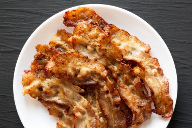 Siyah bir yüzey üzerinde beyaz bir tabakta ev yapımı domuz pastırması. Yukarıdan, dümdüz uzanmış.